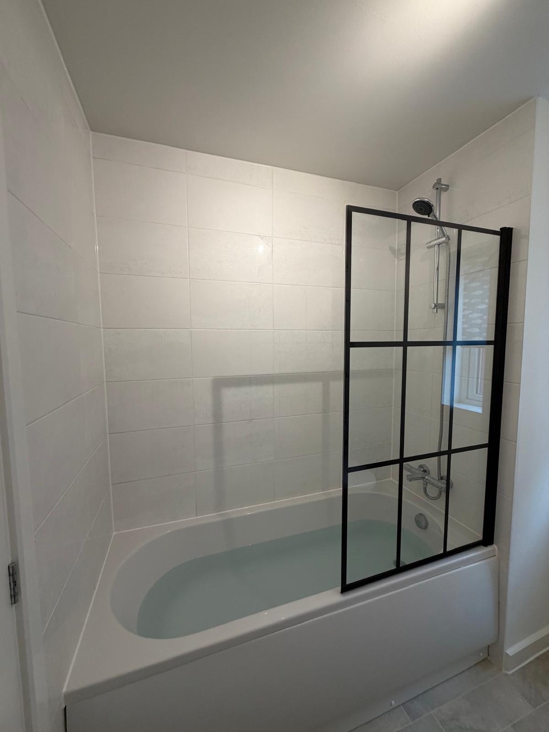 White-tiled bathroom with over-bath shower and black crittall-style glass screen