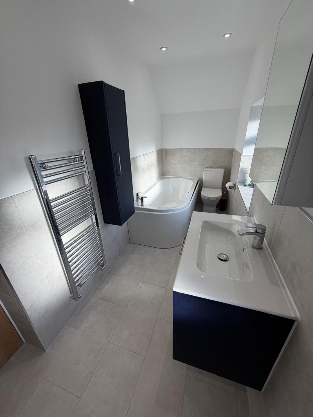 Family bathroom with corner bath, navy vanity units and chrome heated towel rail