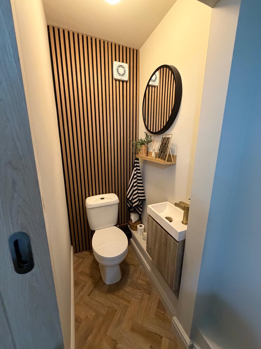 Downstairs cloakroom with oak slat feature wall, round mirror and herringbone floor